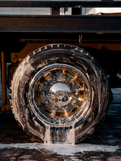 Close-up shot of a truck tire with soap suds running down the sidewall, set against a black truck body and a paved surface.