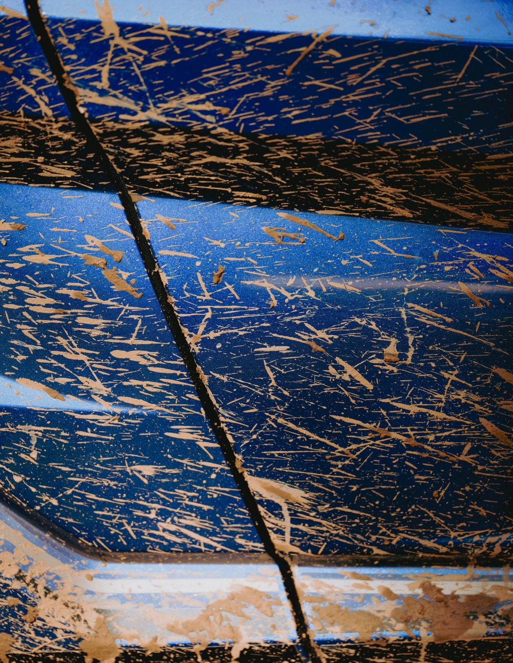 Close-up of a textured blue surface covered in splattered brown mud, creating an abstract pattern with a diagonal dividing line.