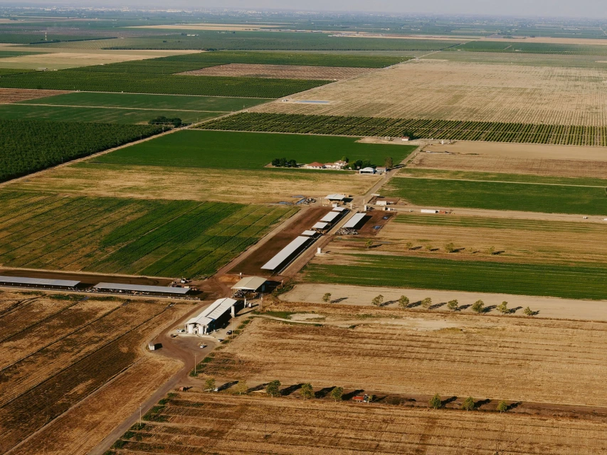 Aerial view of a rural landscape featuring agricultural fields and farm buildings under a clear sky on a sunny day.