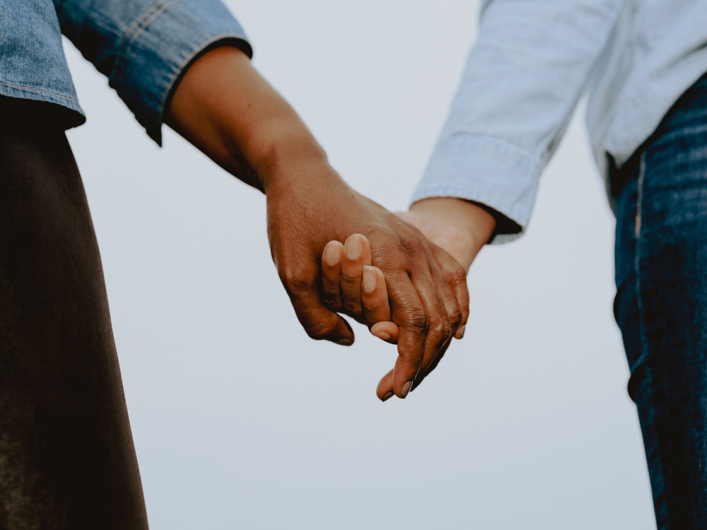 Close-up of two people holding hands against an overcast sky background.