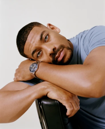 Close-up portrait of a Black man resting head on crossed arms, wearing a blue t-shirt and steel watch.