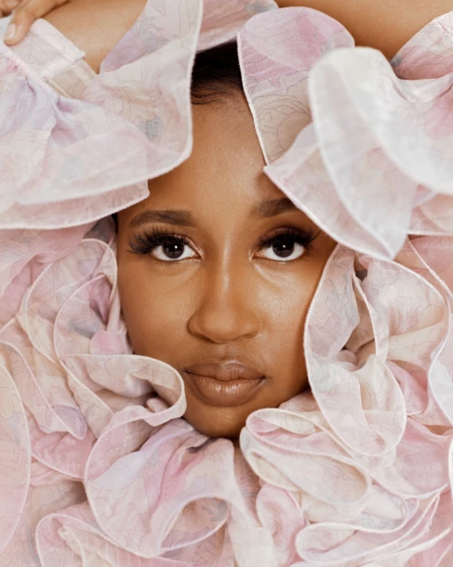 Close-up of a Black woman surrounded by a large pink and white ruffled collar, posing in a photo studio with soft, diffused lighting.