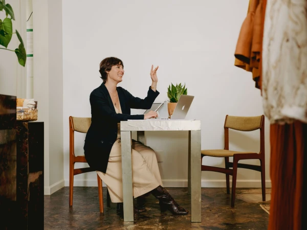Woman in dark blazer seated at table with laptop gesturing during photography by Peyton Fulford