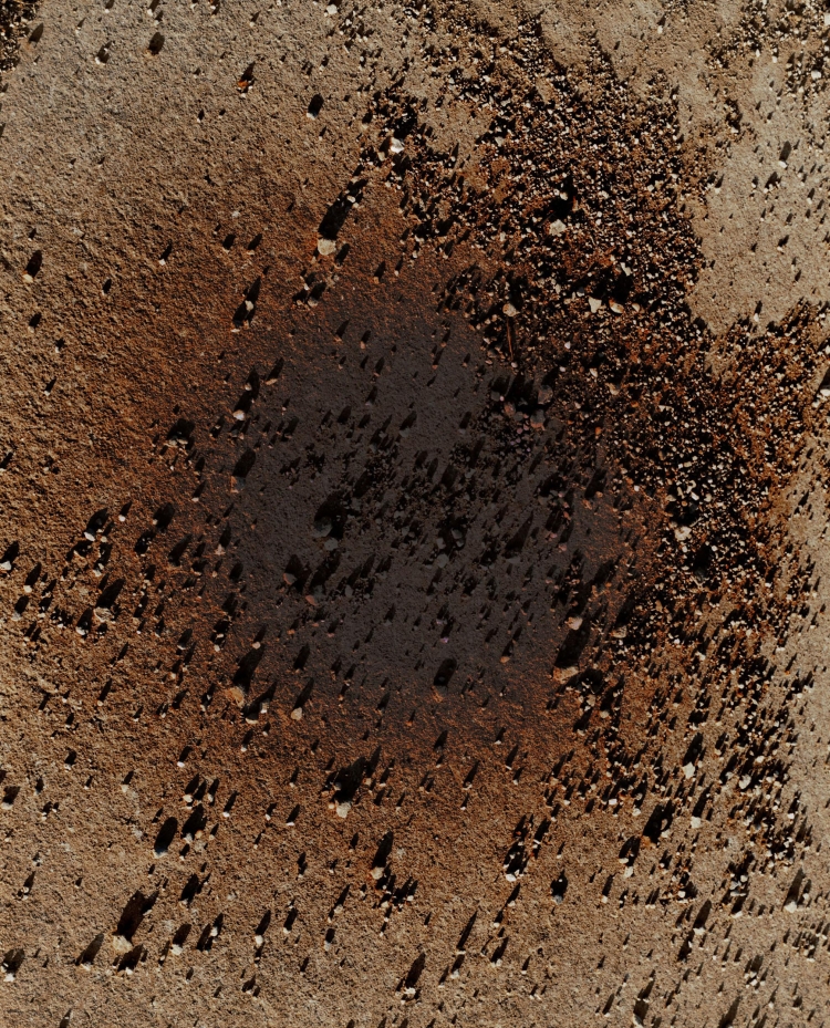 Aerial shot of sun-baked soil with scattered rocks and pebbles, displaying a textured surface in varying shades of brown and dark patches.