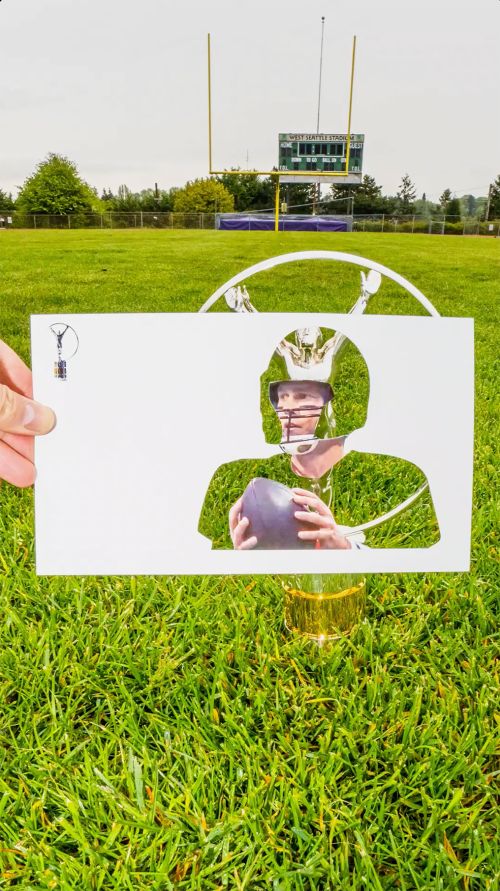 Conceptual outdoor shot of a football quarterback cut-out in a white paper over lush green grass with a football field in the background.