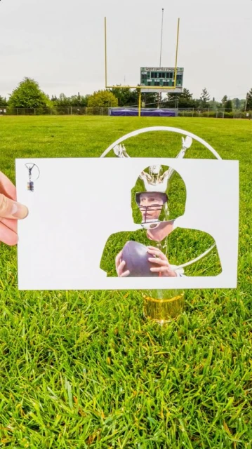 Conceptual outdoor shot of a football quarterback cut-out in a white paper over lush green grass with a football field in the background.