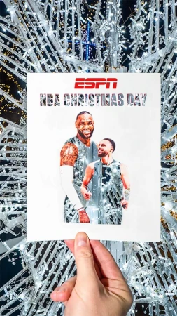 Close-up of a hand holding an ESPN NBA Christmas Day poster featuring basketball players against a white and silver Christmas light background.