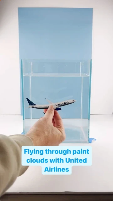 Close-up shot of a United Airlines toy plane in clear water inside a rectangular glass tank, held by a person's hand.