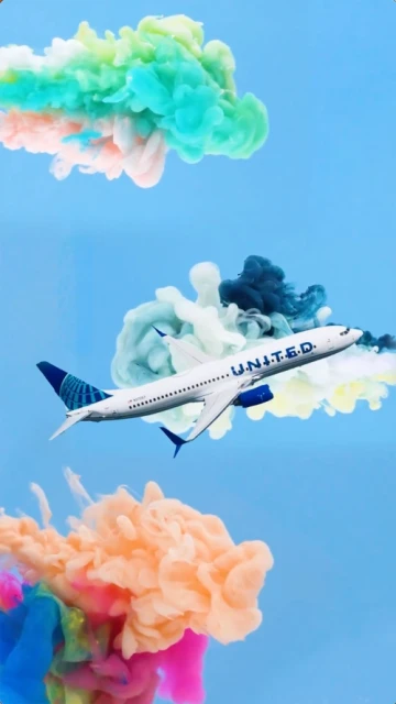 Airplane with United Airlines logo ascends through an abstract sky with colorful smoke clouds; vibrant and surreal composition.