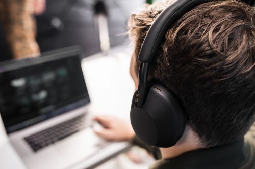 Person wearing black Sony headphones and using a laptop. Close-up shot of technology and a user at a computer.