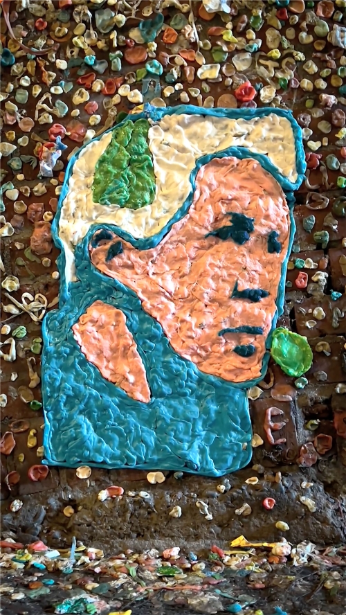 Close-up of a portrait art piece on a brick wall, created from brightly colored gum, showcasing artistic design and urban creativity.