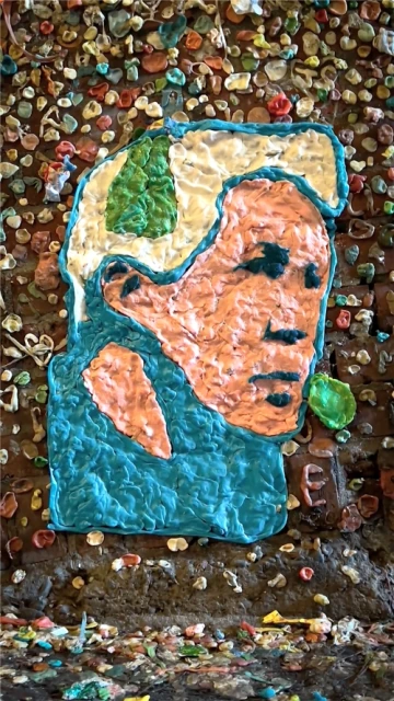 Close-up of a portrait art piece on a brick wall, created from brightly colored gum, showcasing artistic design and urban creativity.