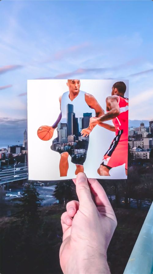Digital collage of basketball players and cityscape. A hand holds an image overlaying an outdoor scene with trees and a cloudy sky.