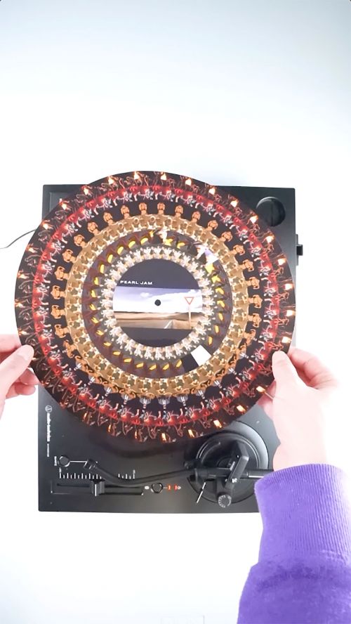 Overhead shot of a record player with a Pearl Jam picture disc, hands visible holding the record on a white background.
