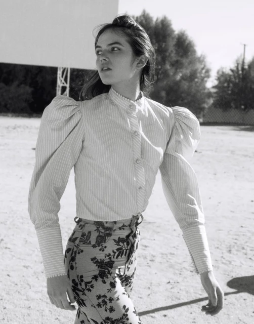 Black and white outdoor shot of a young adult woman in a striped shirt and floral pants looking away from camera.