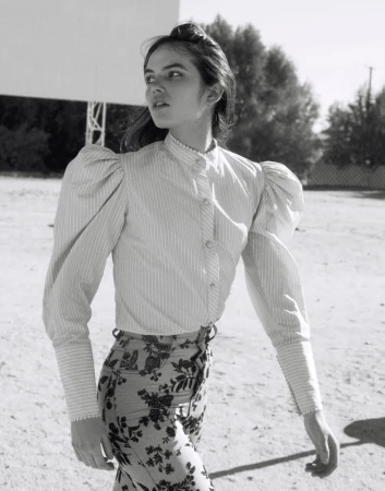 Black and white outdoor shot of a young adult woman in a striped shirt and floral pants looking away from camera.