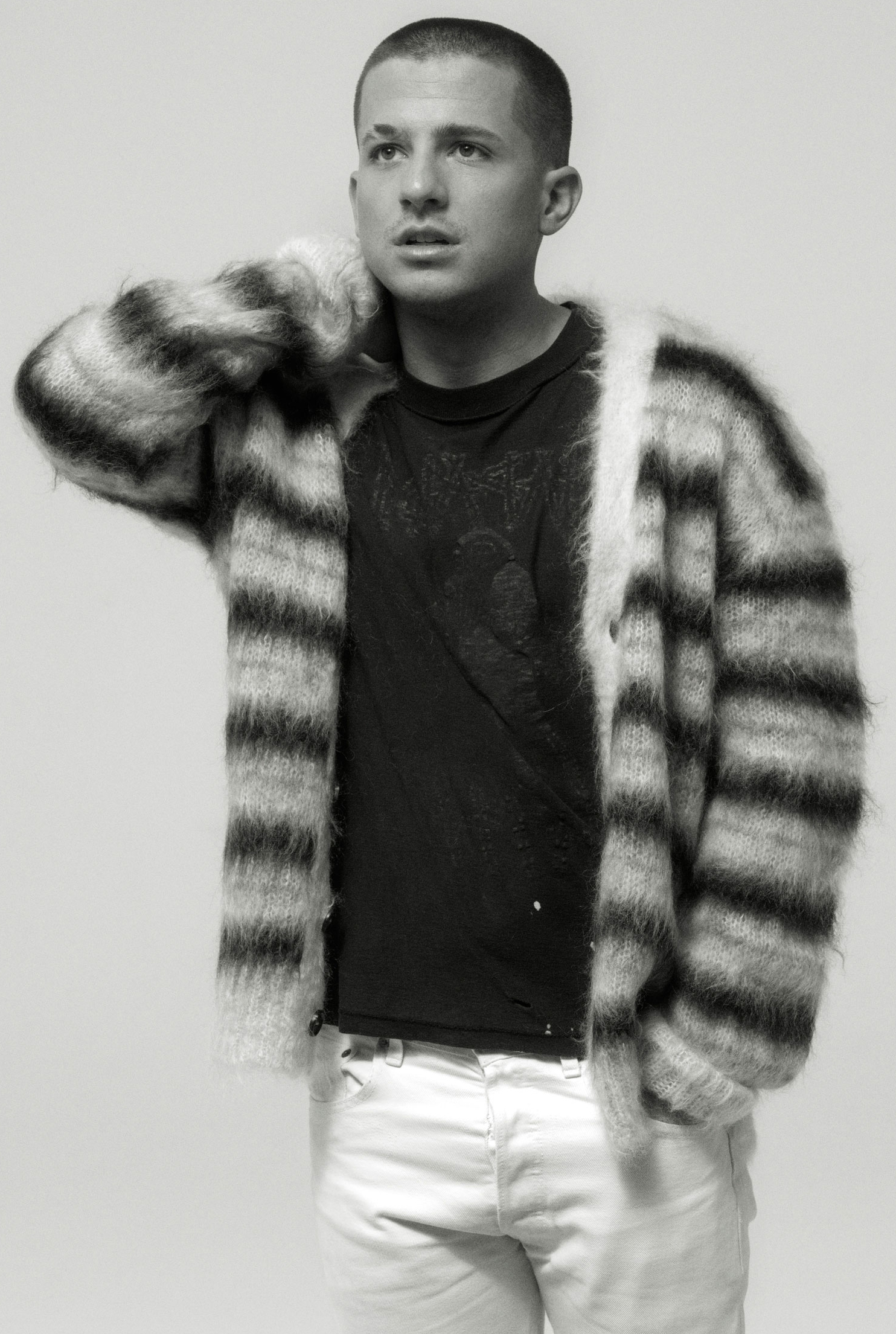 Black and white portrait of a male adult in a striped cardigan, black t-shirt and white pants, posing in a photo studio with a neutral background.