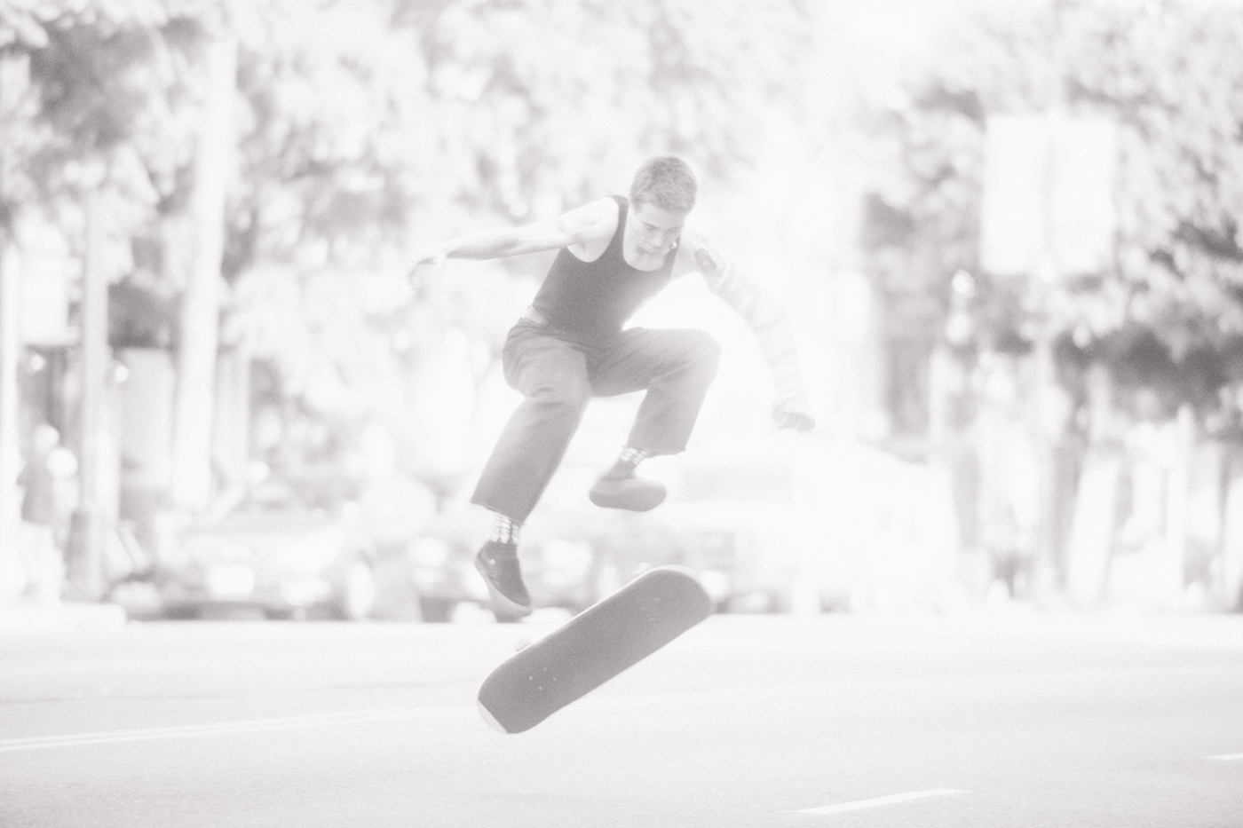 Skateboarder performing an aerial trick over a skateboard on a city street, captured in high-key monochrome by Todd Cole.