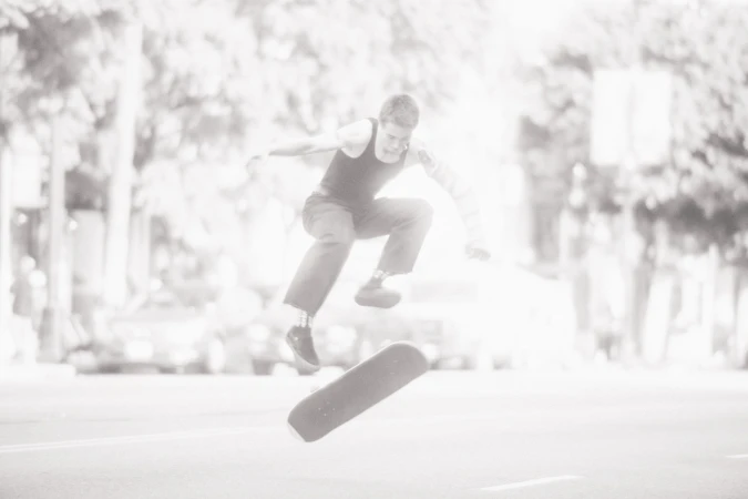 Skateboarder performing an aerial trick over a skateboard on a city street, captured in high-key monochrome by Todd Cole.