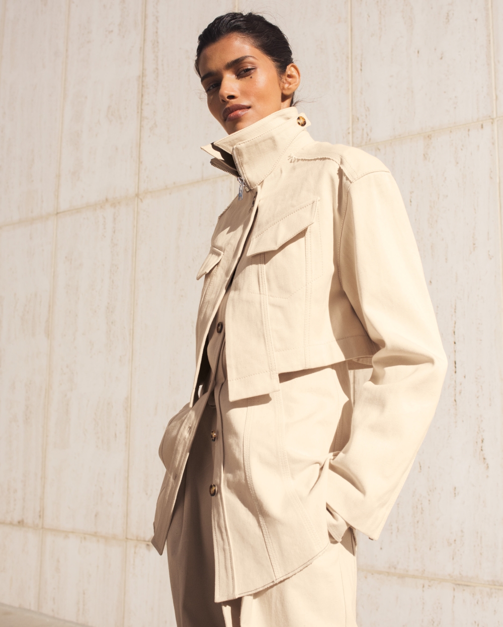 Woman in a beige jacket and pants, posing in front of a neutral wall, medium shot, fashion editorial photography, neutral tones.