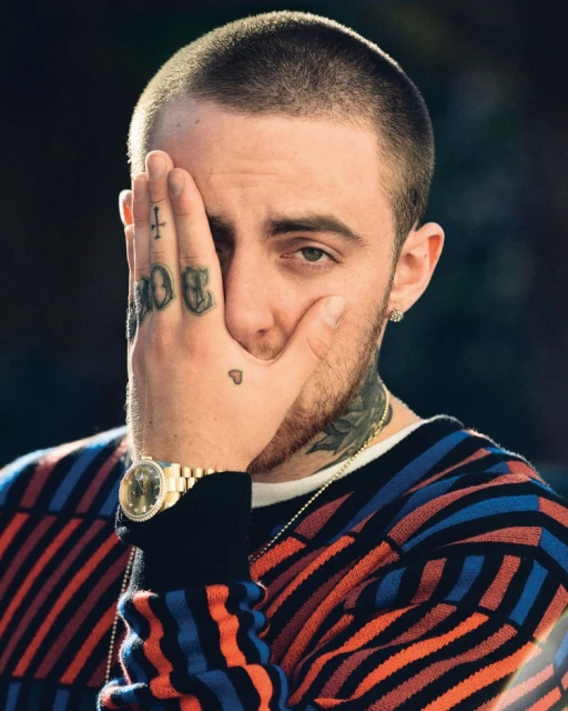 Close-up portrait of a man with hand tattoos covering part of his face, wearing a patterned sweater and a gold watch. 