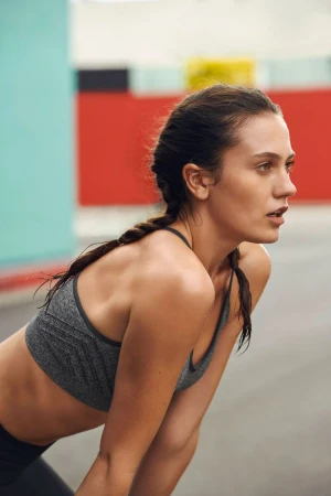 Close-up profile of a woman in a grey sports bra with braided hair leaning forward outdoors in Los Angeles.