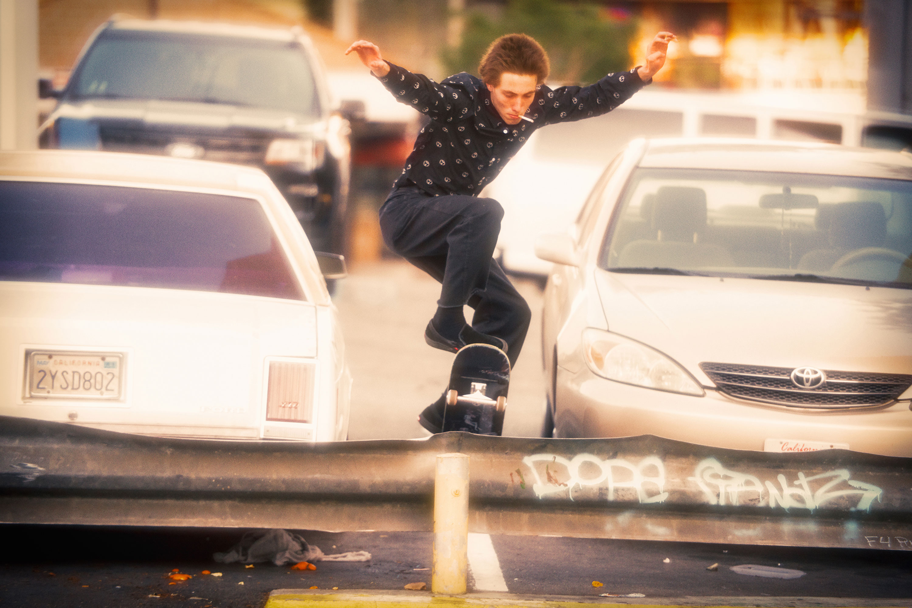 Skateboarder performs a trick on a metal barrier in an urban setting, cars in the background, focusing on urban lifestyle and action.