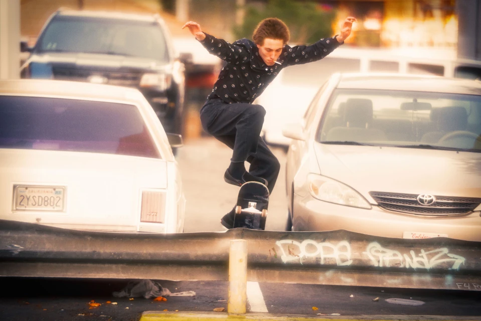 Skateboarder performs a trick on a metal barrier in an urban setting, cars in the background, focusing on urban lifestyle and action.