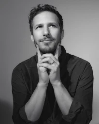 Portrait of Andy Samberg resting his chin on his hands with a pensive expression, captured by photographer Todd Cole.