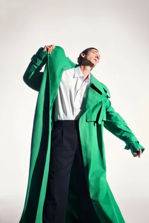 Man wearing a vibrant green trench coat over a white shirt and black trousers against a white studio background.