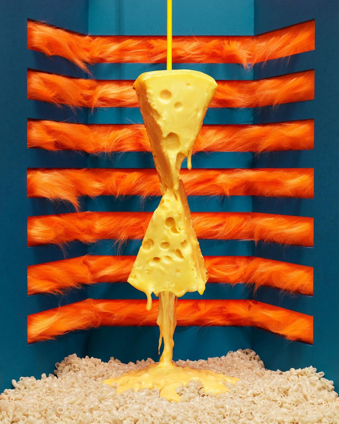 Cheese slices arranged like an hourglass over a pile of pasta with an orange fringed background, creating a playful food scene.