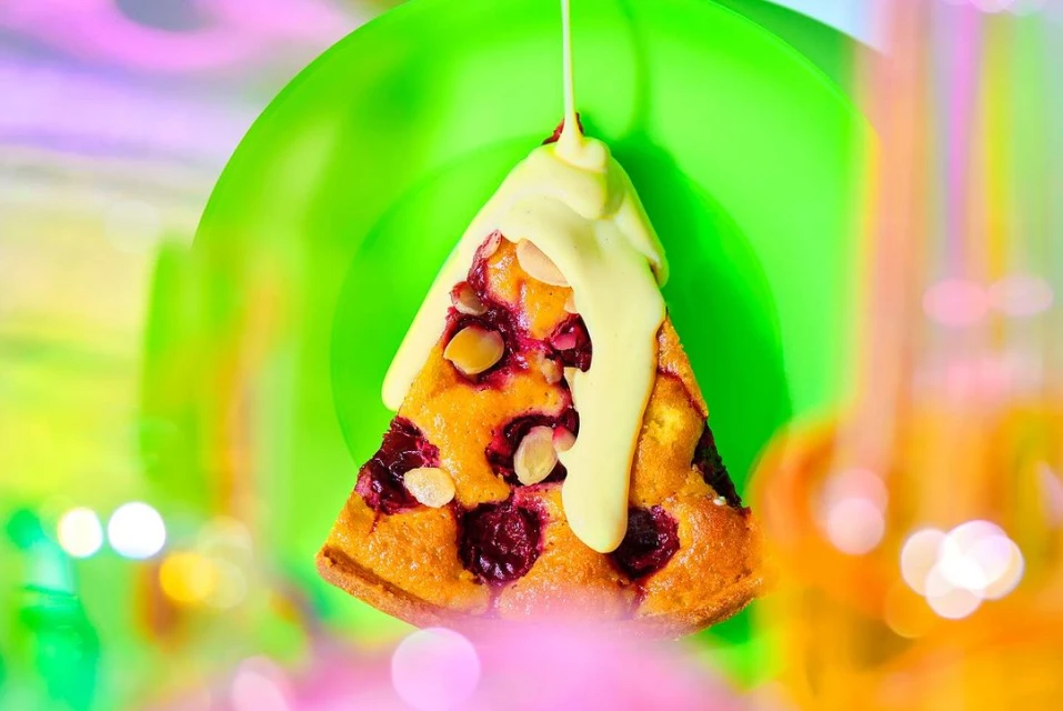 Bright, eye-level food photography of a slice of cherry cake with white sauce drizzle, showcasing vibrant colors and a dessert theme.
