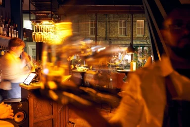 Long exposure bar interior scene in London captured by Richard Wadey with blurred figures and glowing amber lights.