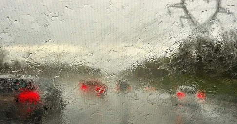 Rain-streaked windshield with blurred glowing red car taillights in the background