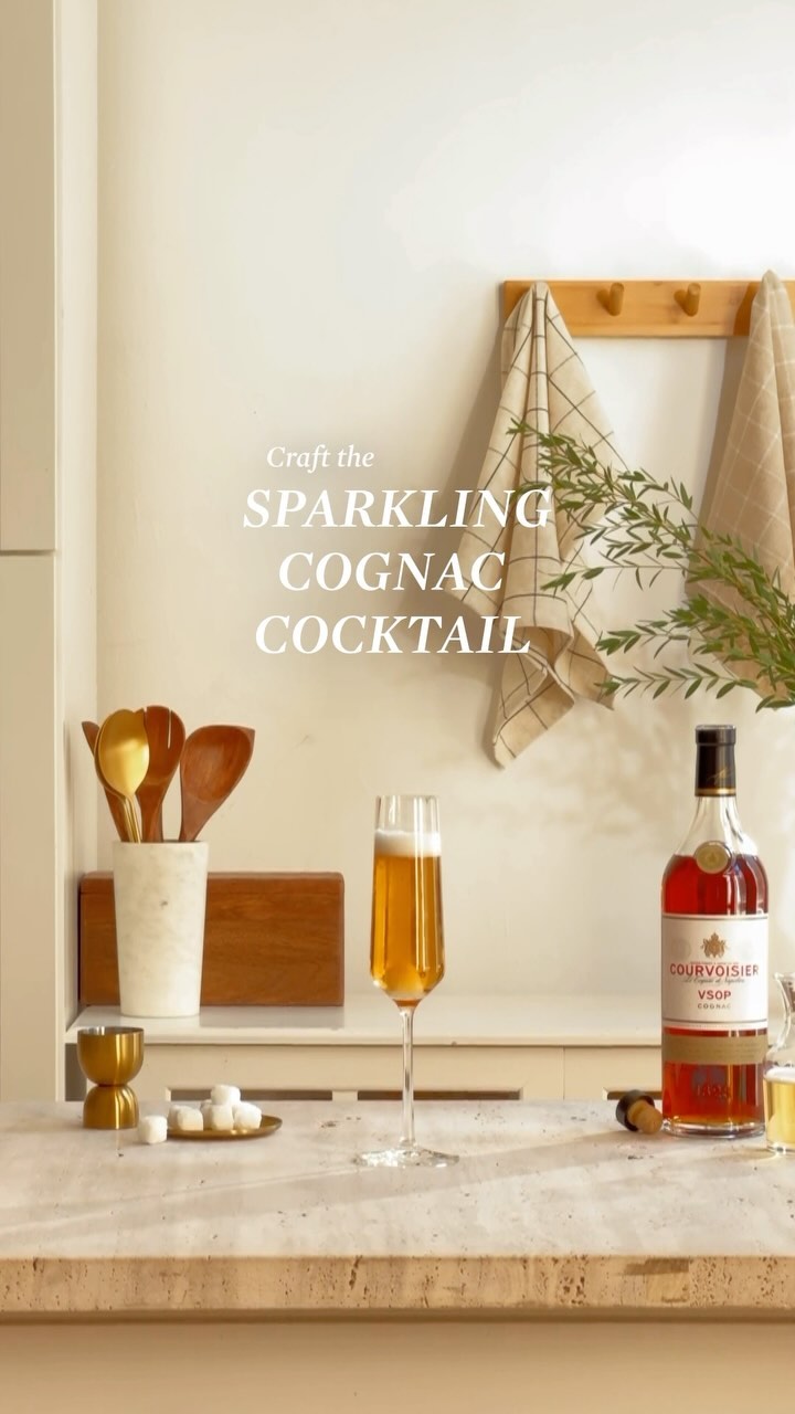 Still life with champagne flute, liquor bottle, sugar cubes, and kitchenware arranged on a kitchen counter with neutral background and towels.