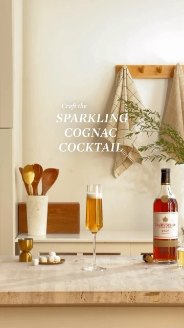 Still life with champagne flute, liquor bottle, sugar cubes, and kitchenware arranged on a kitchen counter with neutral background and towels.
