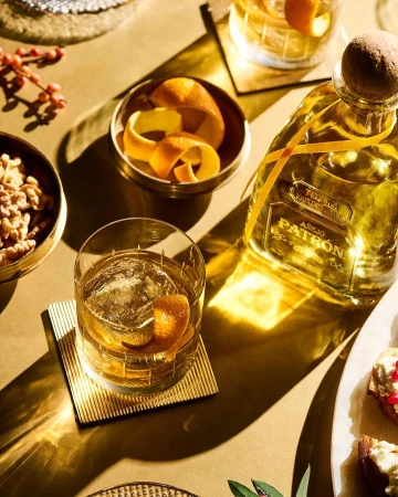 Elegant display of tequila añejo in a clear bottle, alongside a crafted cocktail with an orange peel garnish and toasted appetizers.