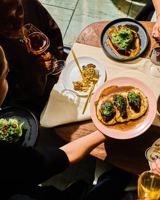 Overhead shot of a brunch table with various plates of food, including pancakes and salads, accompanied by wine and water glasses.