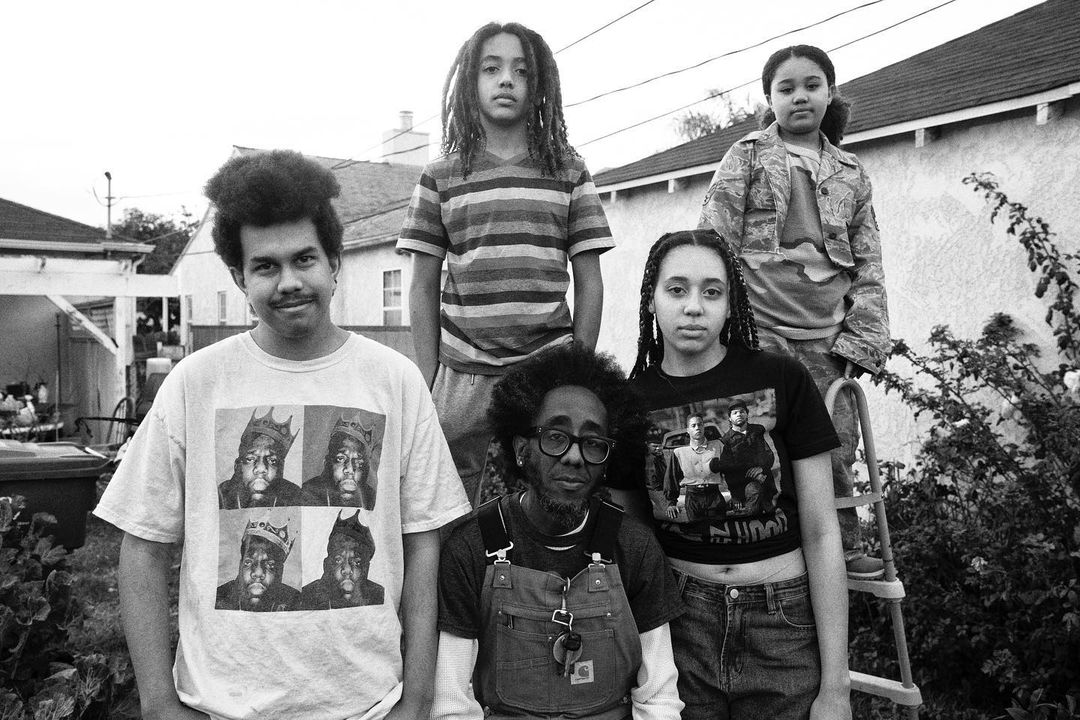 Black and white photograph capturing a diverse group of five people posing outdoors in casual outfits against a suburban backyard backdrop.