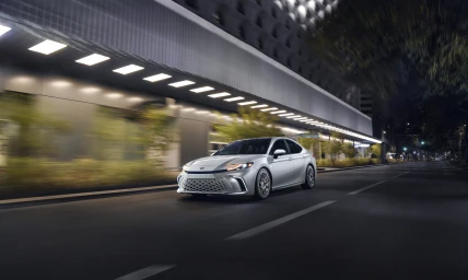 Silver car driving on a dark city street at night with motion blur on buildings