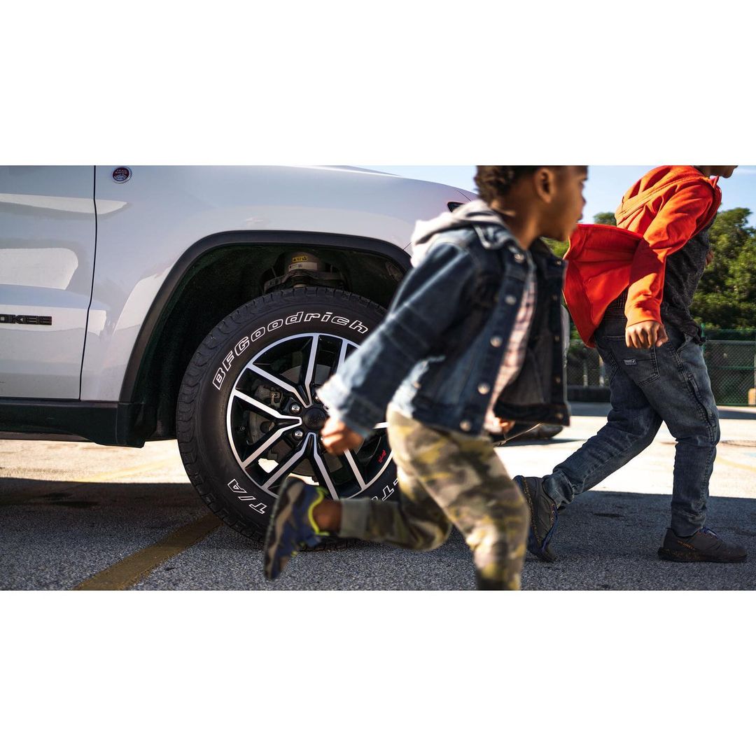Two children run across a parking lot in front of a silver SUV, capturing a dynamic scene with a focus on the vehicle and the children's motion.