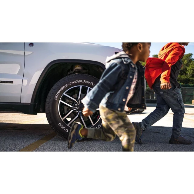 Two children run across a parking lot in front of a silver SUV, capturing a dynamic scene with a focus on the vehicle and the children's motion.