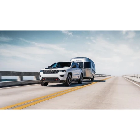 White Jeep Grand Cherokee towing a silver Airstream trailer on a highway under a blue sky. Automotive and travel lifestyle imagery.