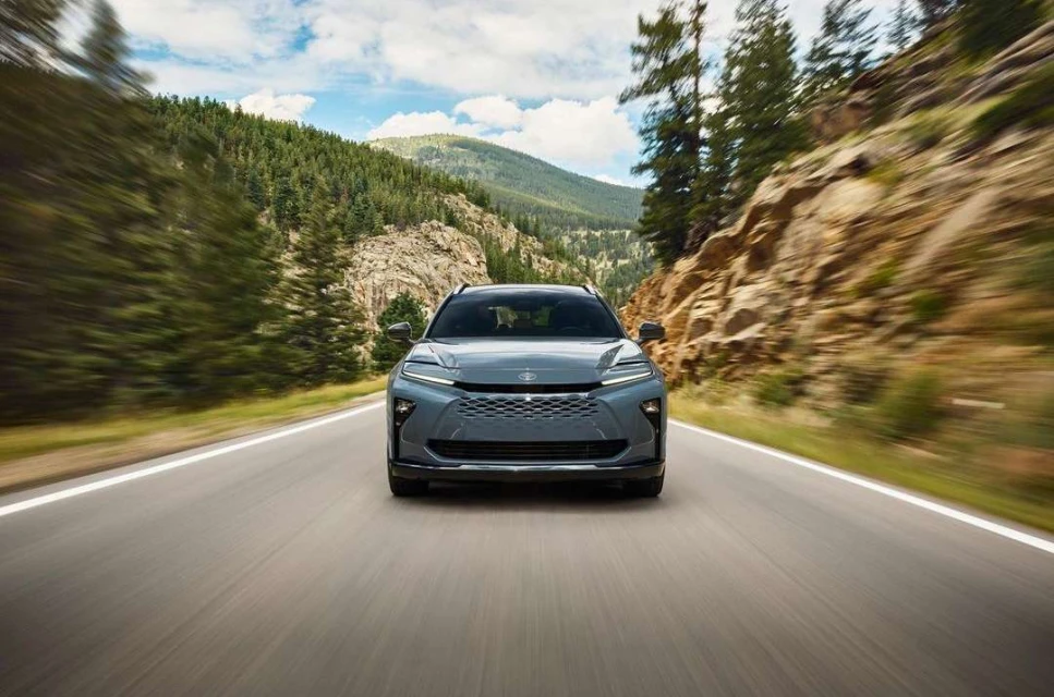 Grey car driving on asphalt road with mountain range and forest background under blue sky with clouds, motion blur effect.