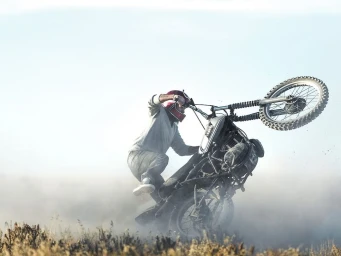 A rider performing a wheelie on a dirt bike in a dusty outdoor landscape, captured by Johnny Valentine.