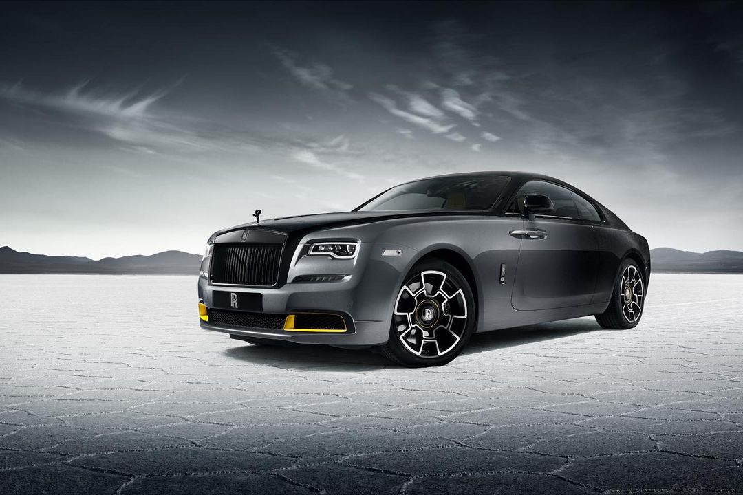 Sleek grey Rolls-Royce Wraith coupe on a vast salt flat under dramatic sky, highlighting luxury automotive design and elegant details.