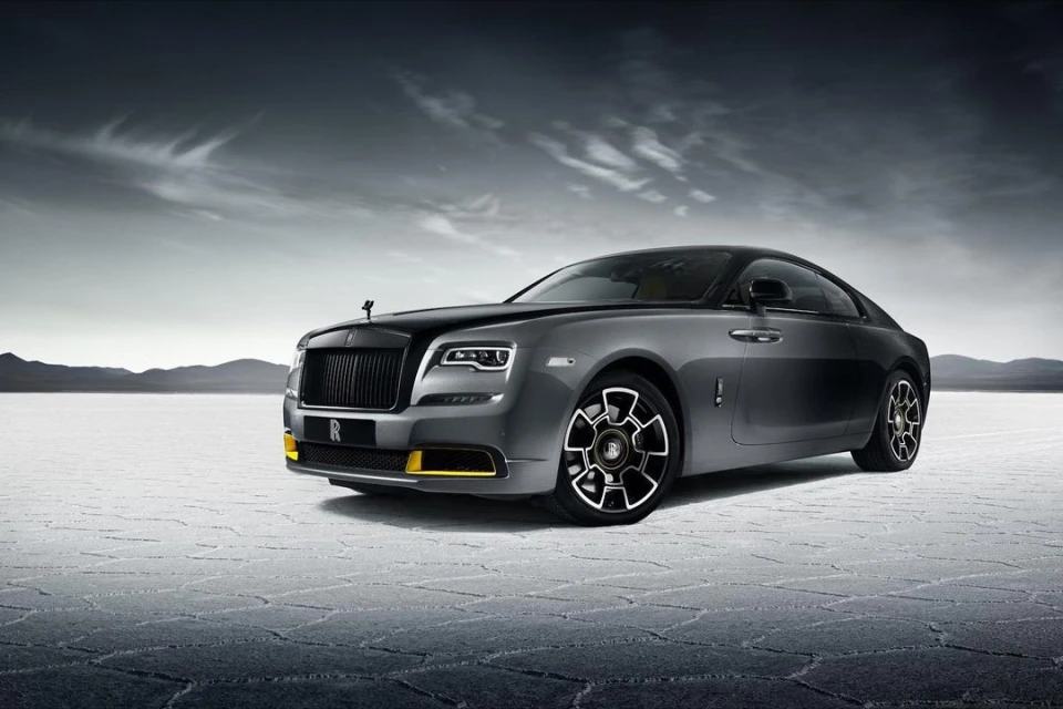 Sleek grey Rolls-Royce Wraith coupe on a vast salt flat under dramatic sky, highlighting luxury automotive design and elegant details.