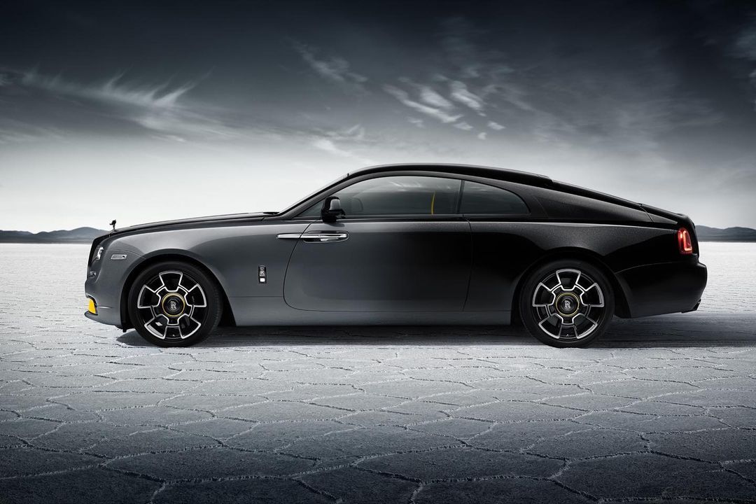 Luxury Rolls-Royce coupe in two-tone black and gray, parked on a cracked salt flat against a stormy sky. Automotive excellence.