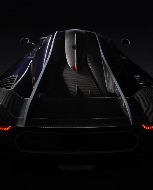 Rear view of a dark blue and black Koenigsegg Jesko sports car with visible carbon fiber detailing in a low-key lighting setup.