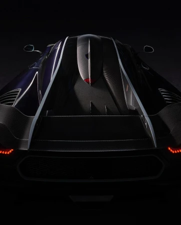 Rear view of a dark blue and black Koenigsegg Jesko sports car with visible carbon fiber detailing in a low-key lighting setup.